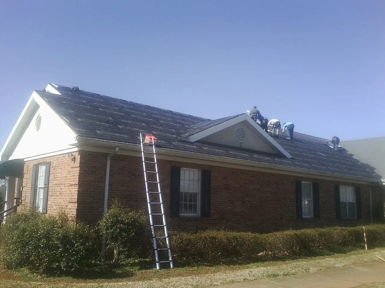 Crew tearing shingles off a brick ranch roof with a ladder set — Emergency Roof Repair work by our crew in Nappanee