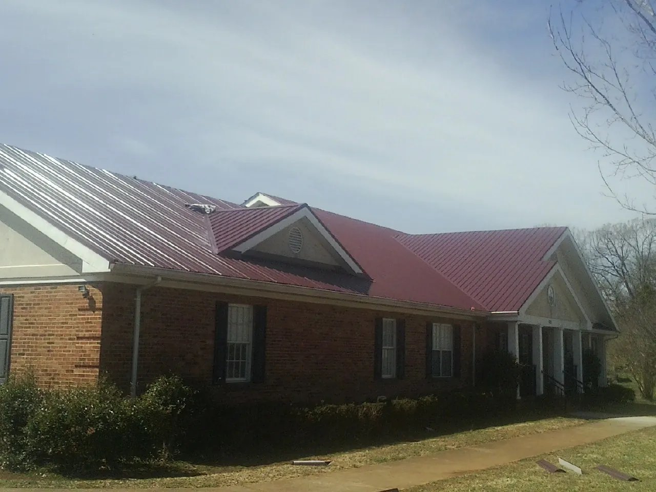 Red metal roof with gabled entries on a long brick building, from a Hail Damage Roof Repair job in Nappanee