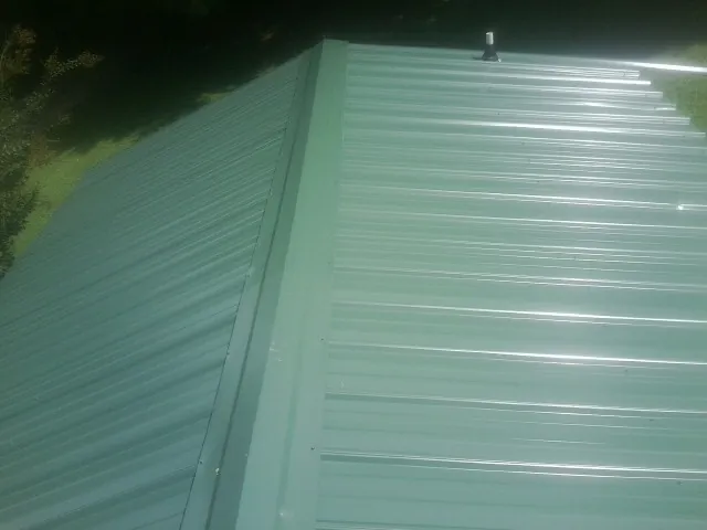 New green metal panels meeting at the ridge of a roof — Flat Roof Repair work by our crew in Nappanee