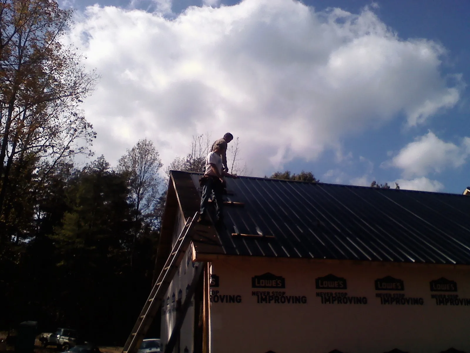 Roofer fastening dark metal panels high against a cloudy sky, from a Roof Inspection job in Nappanee