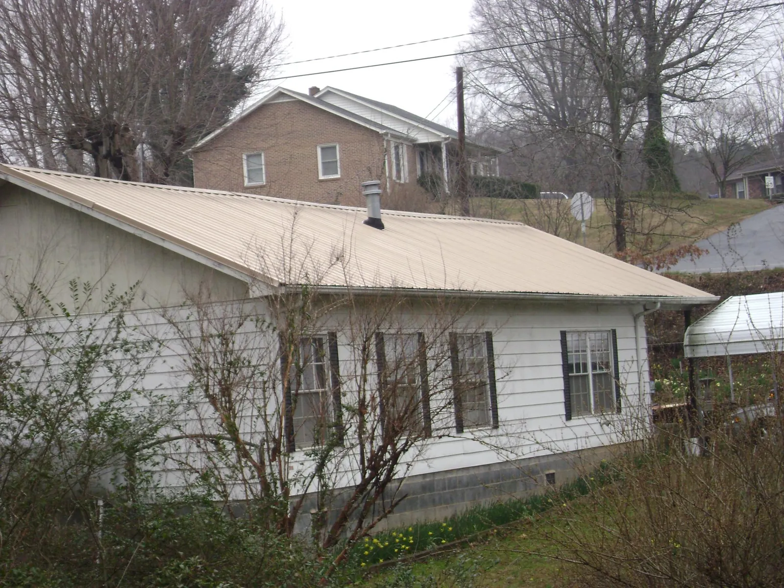 Tan metal roof on a white sided house set into a hillside — Commercial Roofing by Roofing Brothers in Nappanee